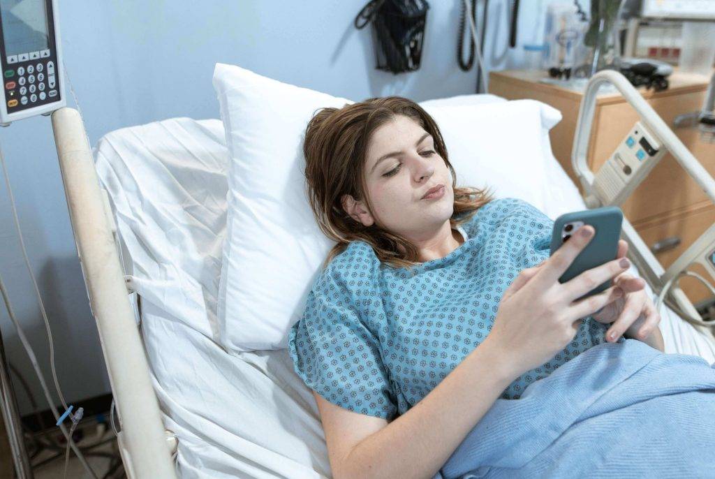 woman on phone resting in hospital bed