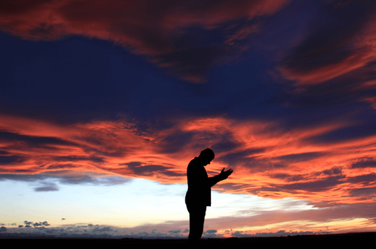 man praying outside under sunrise clouds